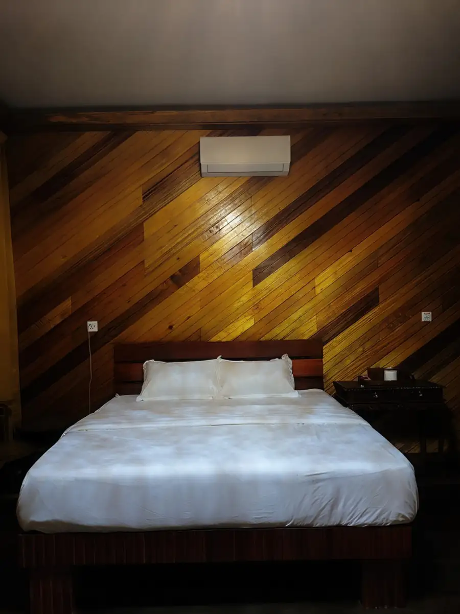 A cozy bedroom at Noura Resort near Pulau Bum Bum featuring a large bed, warm diagonal wooden plank walls with dark polished hardwood floors, and air con.