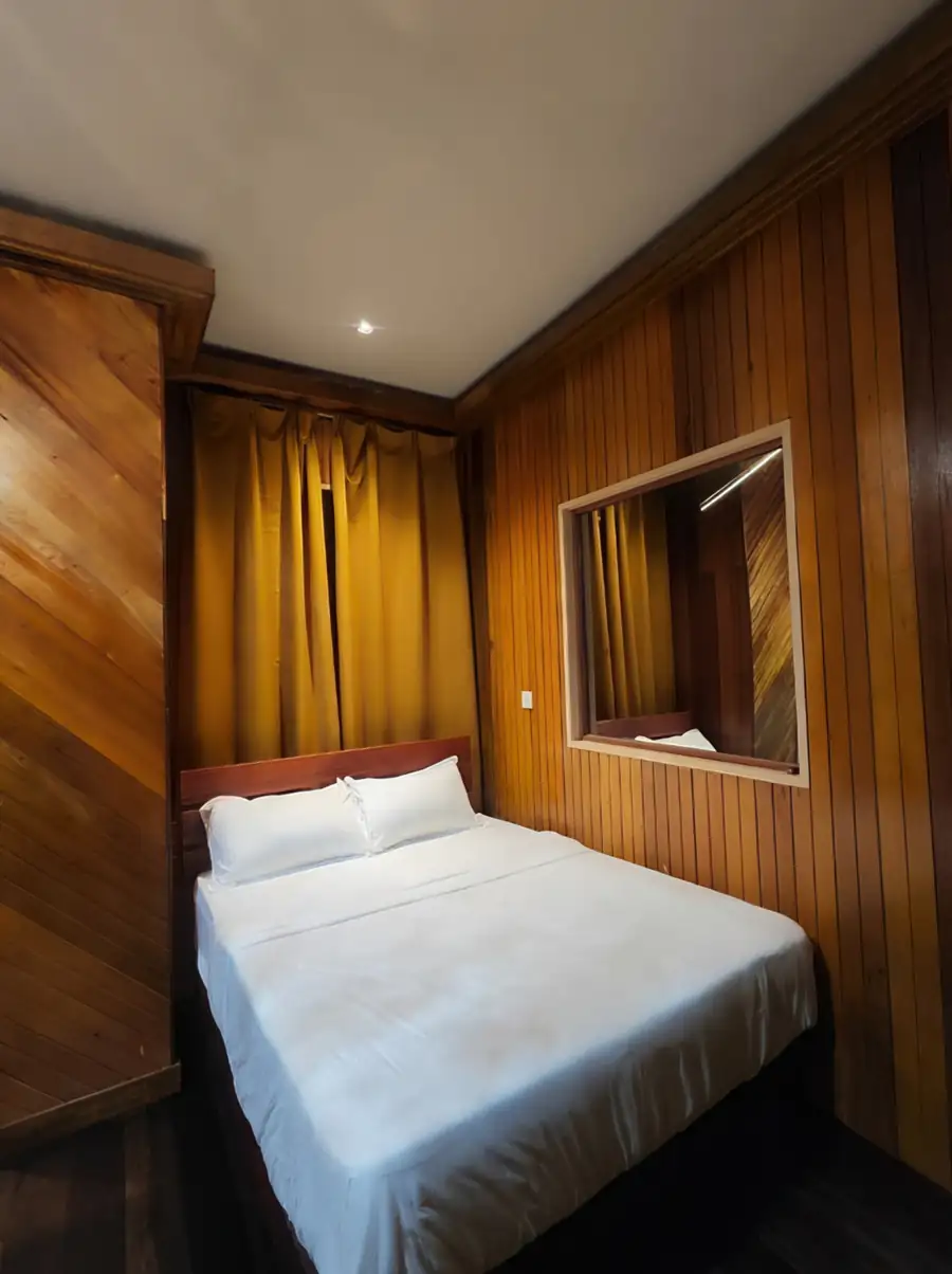 A comfortable bedroom at Noura Resort in the Tun Sakaran Marine Park featuring a cozy bed, yellow curtains, authentic timber walls with dark wood flooring, and A/C.